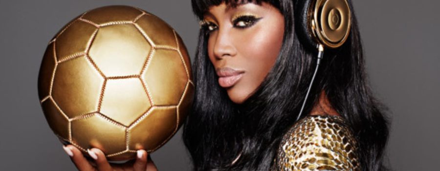 A woman in gold and headphones holding a soccer ball.
