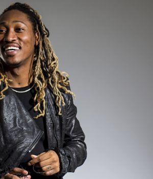 A man with dreads is smiling and wearing a leather jacket.