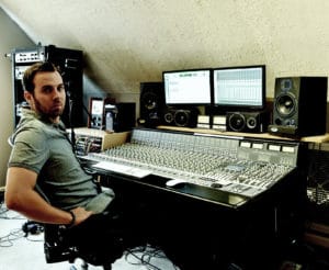 A man sitting in front of a large sound board.